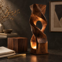 Corner detail of twisted wooden block floor lamp with an oval window and glowing base opening beside wood, brass and linen samples