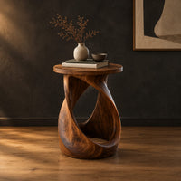 Twisted side table with a circular top and open loop base in a dark studio against a charcoal plaster wall