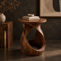 Corner detail of twisted side table with a circular top and open loop base beside wood, brass and linen samples