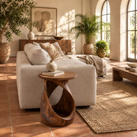 Twisted side table with a circular top and open loop base in a bright living room with arched windows and plants