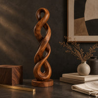 Corner detail of twisted wood sculpture of two intertwined loops with a flat disc foot beside wood, brass and linen samples
