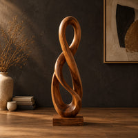 Twisted figure eight wood sculpture with two open loops on a block base in a dark studio against a charcoal plaster wall