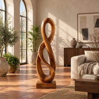 Twisted figure eight wood sculpture with two open loops on a block base in a bright living room with arched windows and plants