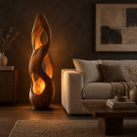 Tall twisted wooden floor lamp with open cutouts that glow warm amber in a dark living room at golden hour