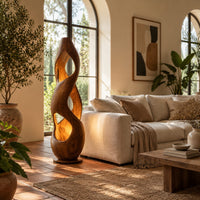 Tall twisted wooden floor lamp with open cutouts that glow warm amber in a bright living room with arched windows and plants