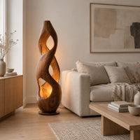 Tall twisted wooden floor lamp with open cutouts that glow warm amber in a Scandinavian living room with white walls