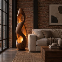 Tall twisted wooden floor lamp with open cutouts that glow warm amber in an industrial loft living room with exposed brick