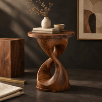 Corner detail of twisted hourglass side table with a thin flat top and open waist beside wood, brass and linen samples