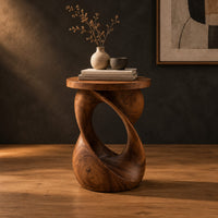 Side table with a circular top on a twisted open loop base in a dark studio against a charcoal plaster wall