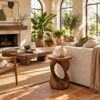Side table with a circular top on a twisted open loop base in a bright living room with arched windows and plants