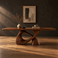 Dining table with a rectangular top on a twisted loop pedestal in a dark studio against a charcoal plaster wall