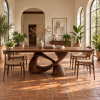 Dining table with a rectangular top on a twisted loop pedestal in a bright dining room with arched windows and plants
