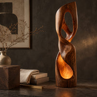 Corner detail of twisted floor lamp with open loops and a glowing hollow base beside wood, brass and linen samples