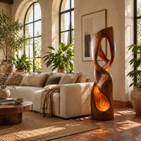 Twisted floor lamp with open loops and a glowing hollow base in a bright living room with arched windows and plants