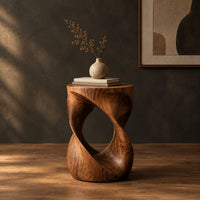 Twisted hourglass side table with an open loop through its body in a dark studio against a charcoal plaster wall