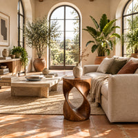 Twisted hourglass side table with an open loop through its body in a bright living room with arched windows and plants