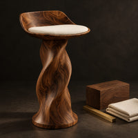 Corner detail of bar stool with a twisted pedestal, a flared foot and a scooped wood seat beside wood, brass and linen samples