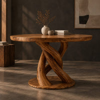 Corner detail of circular wooden dining table with a twisting braided pedestal on a disc base beside wood, brass and linen samples