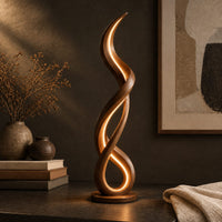 Corner detail of floor lamp of twisting wooden ribbon with a glowing loop at the base beside wood, brass and linen samples