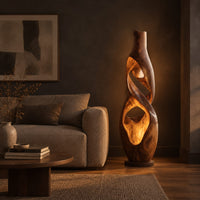 Floor lamp shaped as a twisting vase with open ribbon cutouts that glow in a dark living room at golden hour