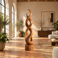 Twisted wood sculpture of intertwined ribbons on a short cylinder base in a bright living room with arched windows and plants