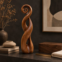 Corner detail of twisted ribbon sculpture with open loops, a spiral top and a dark base beside wood, brass and linen samples