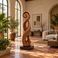 Twisted ribbon sculpture with open loops, a spiral top and a dark base in a bright living room with arched windows and plants