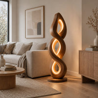 Twisted spiral floor lamp with three glowing loops on a disc base in a Scandinavian living room with white walls