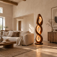 Twisted spiral floor lamp with three glowing loops on a disc base in a bright open plan living room