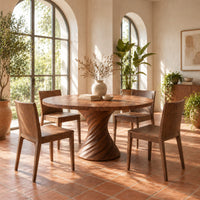 Circular dining table with a twisted spiral hourglass pedestal in a bright dining room with arched windows and plants