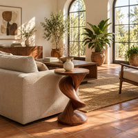 Round side table with a twisting spiral pedestal and a flared base in a bright living room with arched windows and plants