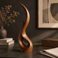 Corner detail of tall twisting flame shaped wood sculpture with an open loop near the base beside wood, brass and linen samples