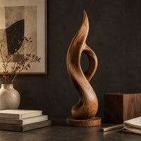 Corner detail of tall twisting flame sculpture with an open loop on a flat disc base beside wood, brass and linen samples