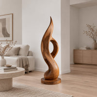 Tall twisting flame sculpture with an open loop on a flat disc base in a Scandinavian living room with white walls