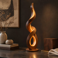 Corner detail of twisting ribbon floor lamp with warm glow inside its loops beside wood, brass and linen samples