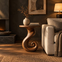 Round side table on a ribbon pedestal that ends in a spiral curl in a dark living room at golden hour