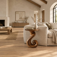 Round side table on a ribbon pedestal that ends in a spiral curl in a bright open plan living room