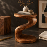 Corner detail of twisting s shape side table with a circular top and wide disc base beside wood, brass and linen samples