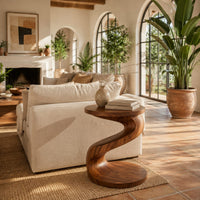 Twisting s shape side table with a circular top and wide disc base in a bright living room with arched windows and plants