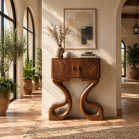 Two door console cabinet on large looping ribbon shaped legs in a bright entryway with arched windows and plants