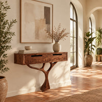 Console table with a two drawer box on a single branching tree pedestal in a bright entryway with arched windows and plants