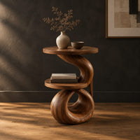 Two tier end table with a spiral ribbon base and a loop foot in a dark studio against a charcoal plaster wall