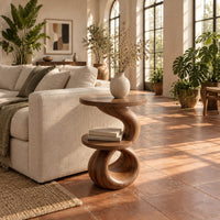 Two tier end table with a spiral ribbon base and a loop foot in a bright living room with arched windows and plants