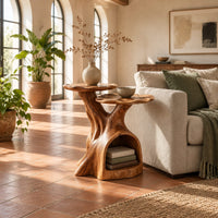 Two tier side table with a trunk base and a hollow for books in a bright living room with arched windows and plants