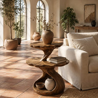 Two tier side table with scalloped tops and a twisting stem in a bright living room with arched windows and plants