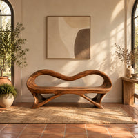 Wooden bench with a wavy looped rim and slender splayed legs in a bright entryway with arched windows and plants
