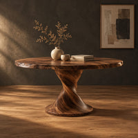 Round dining table on a twisted pedestal with a flared disc base in a dark studio against a charcoal plaster wall