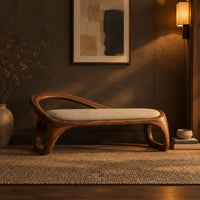 Bench with a padded seat and an arched back rail on open loop legs in a dark entryway at golden hour
