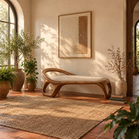 Bench with a padded seat and an arched back rail on open loop legs in a bright entryway with arched windows and plants