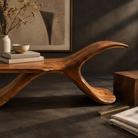 Corner detail of bench with a flat plank seat, a swooping base and an upswept tail beside wood, brass and linen samples